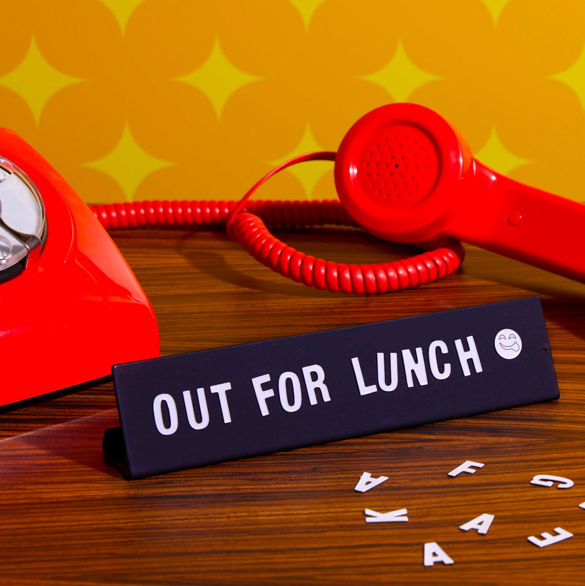 Retro red telephone and desk sign reading 'Out For Lunch' on a wooden office desk