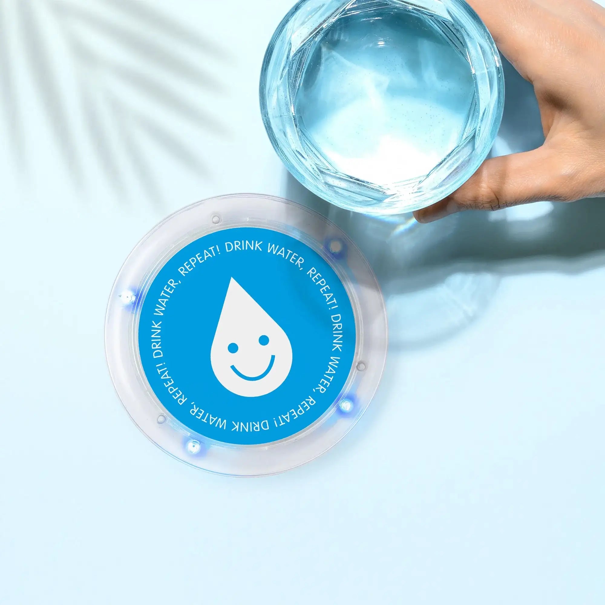 Hand holding glass of water above blue hydration reminder coaster with smiley water drop design