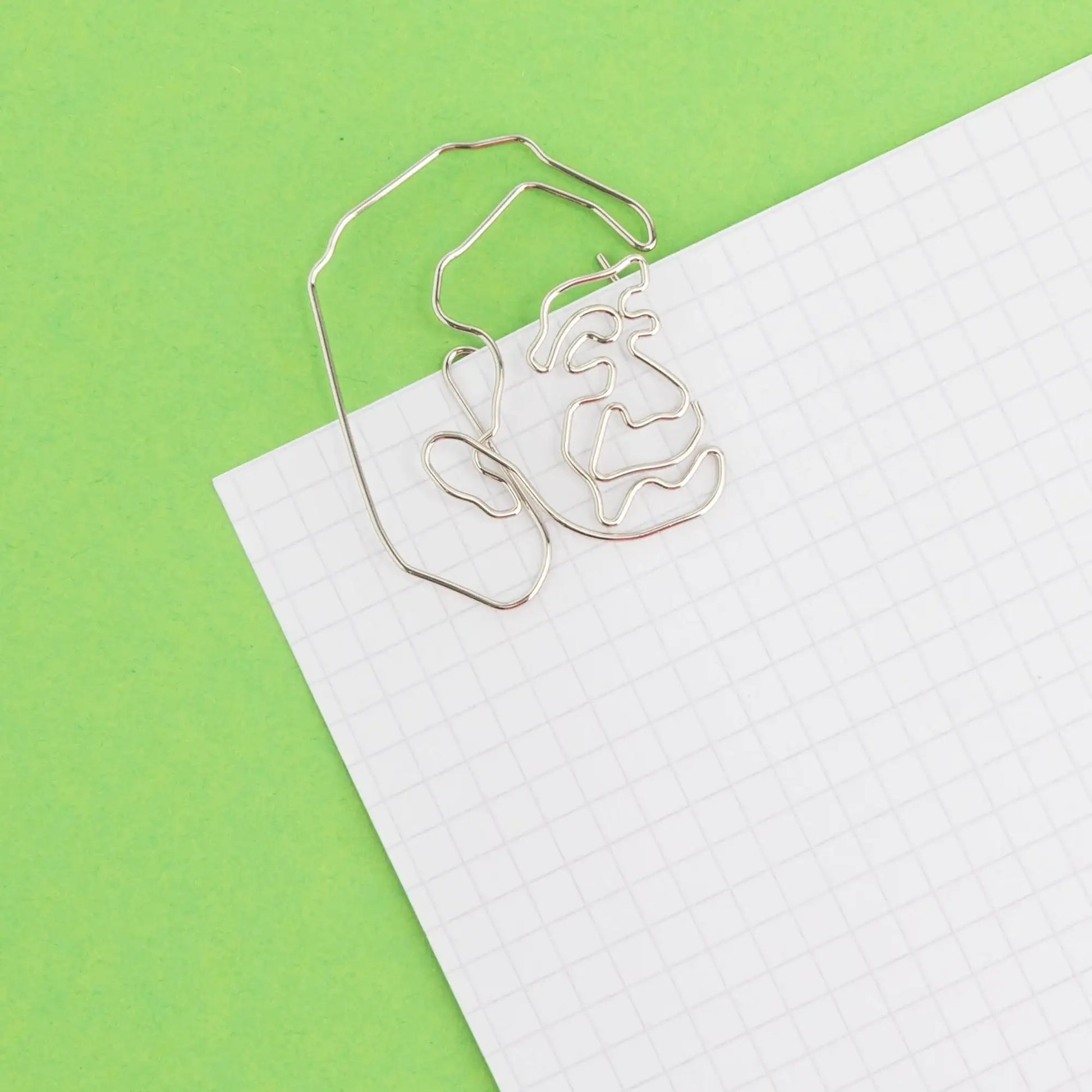 Face-shaped silver paperclip on grid notebook with green background, unique desk accessory.