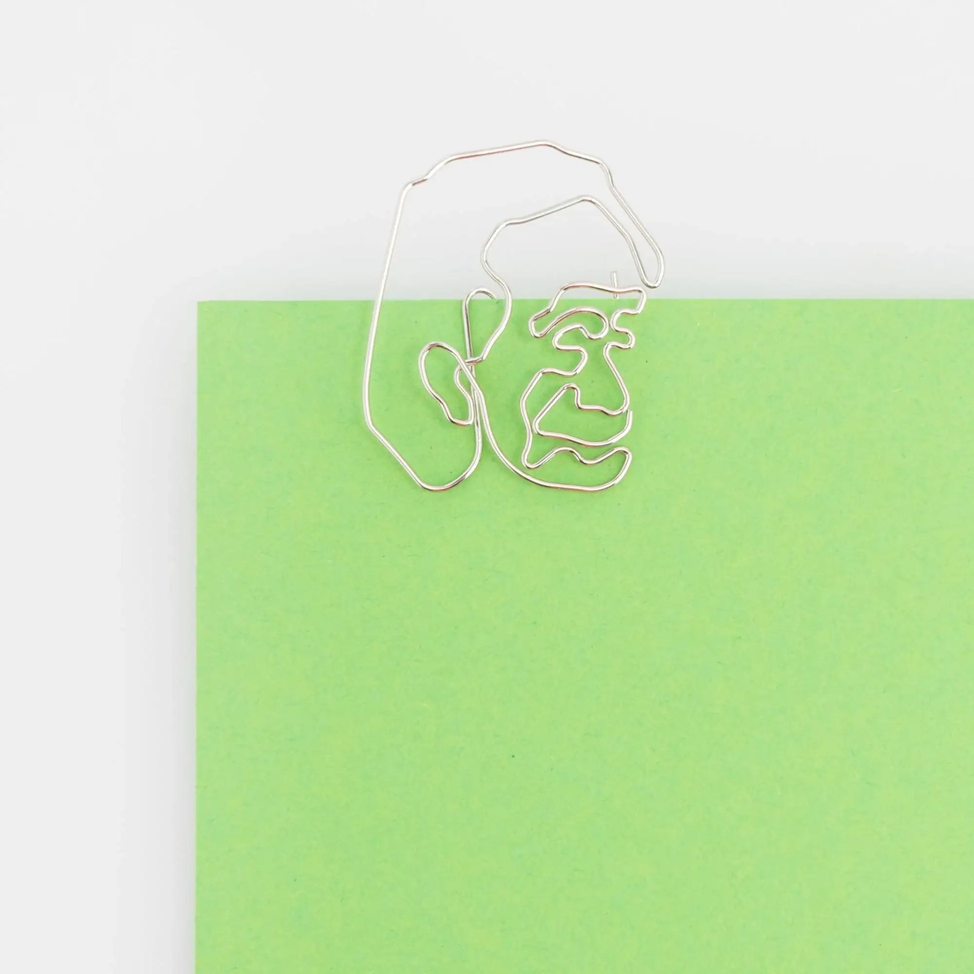Silver paperclip shaped like a face on a green sheet of paper, quirky desk accessory